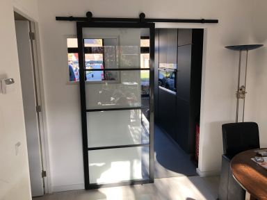 Oss. Ombouwen van benedenverdieping. Woonkamer werd keuken. Keuken werd woonkamer. Skan Trae roldeur als blikvanger tussen woonkamer en keuken. 2019.