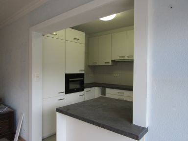 Dezelfde keuken in Lanaken, maar dan afgewerkt. Waar eerst nog een deur naar een gangetje was, staan nu de oven en de frigo.